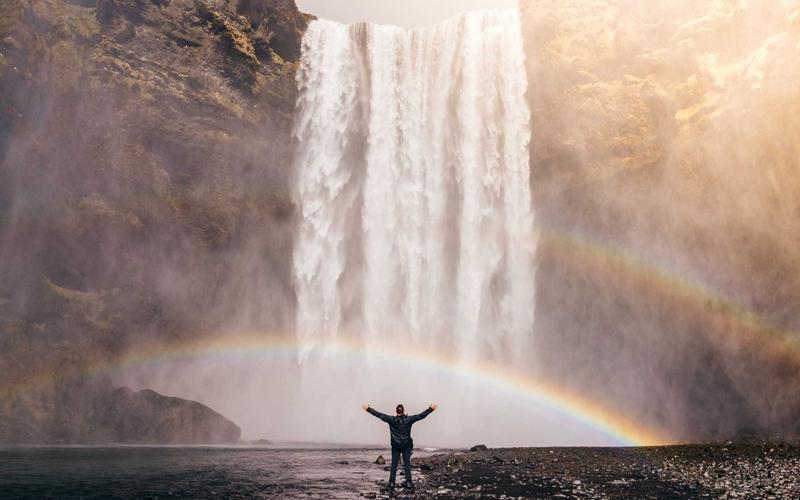 AI-generated image of a hiker standing under a rainbow beside a waterfall